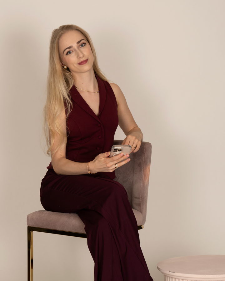 Maureen Evelyn seated on a stool, phone in hand, smiling at the camera